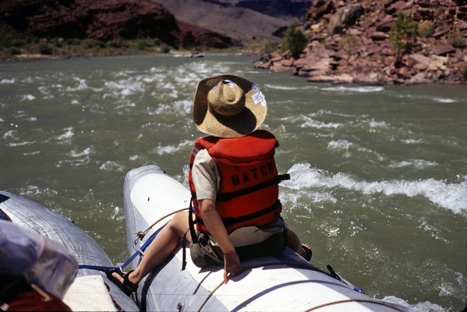 A man in a hat is sitting on the back of a raft.