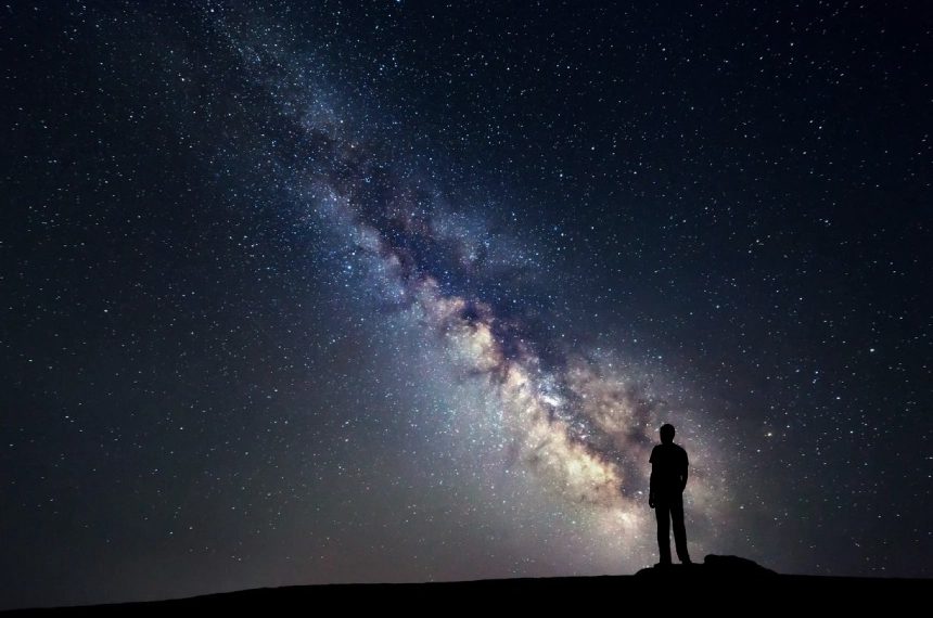 A person standing on top of a hill under a sky filled with stars.