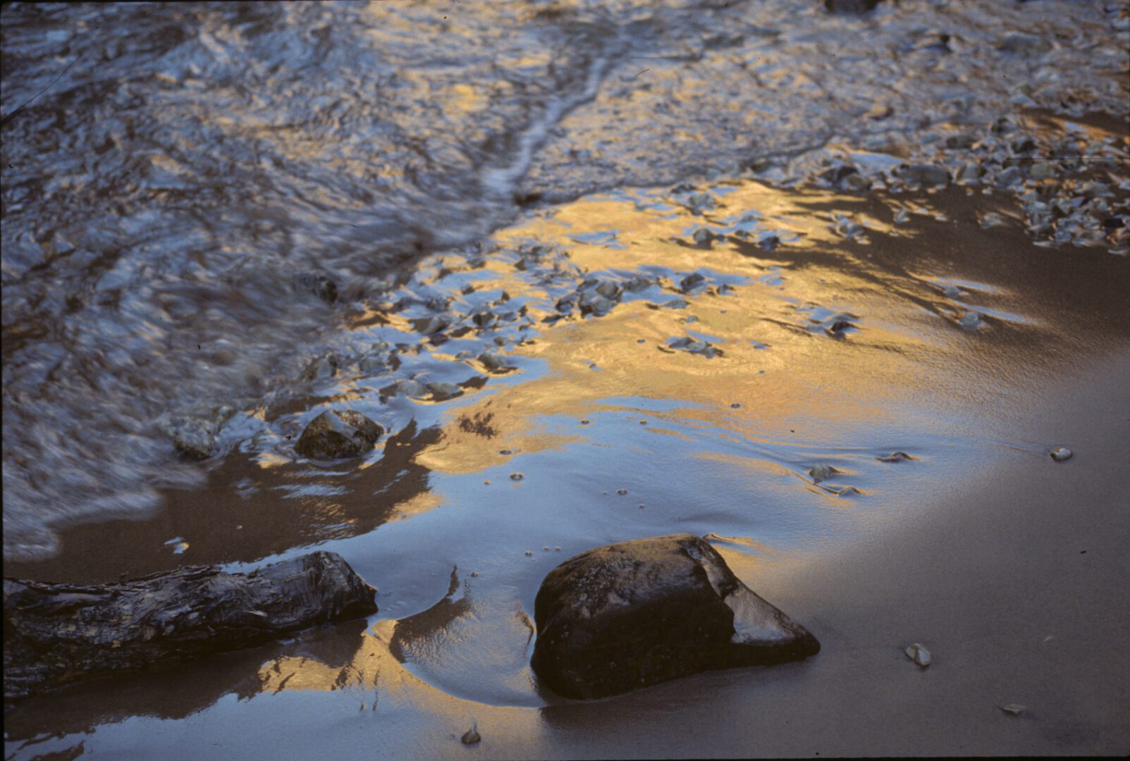 A rock on the beach with water and rocks in the background.